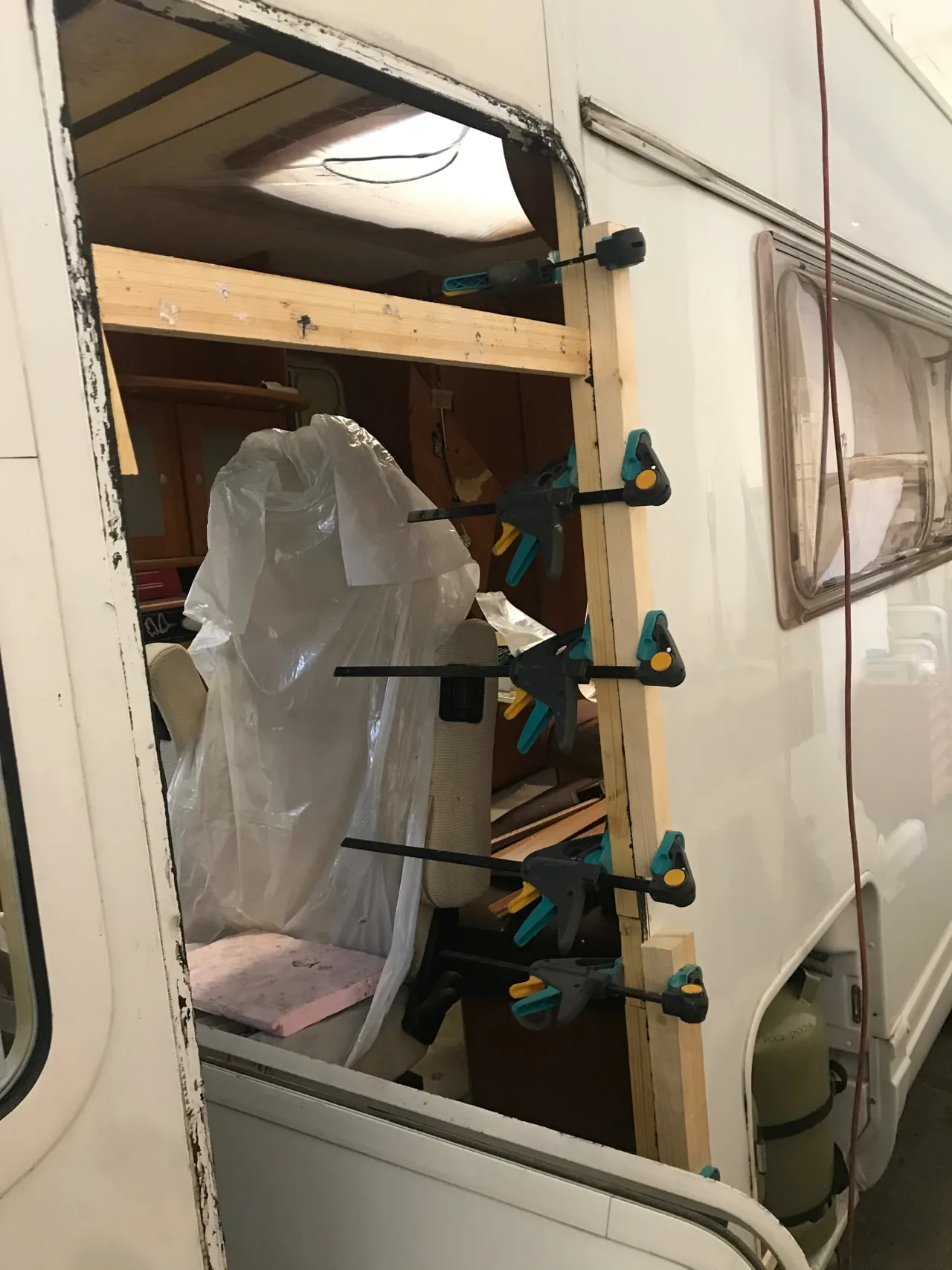 Geöffneter Seitenwandbereich eines Wohnmobils mit Holzleisten und angesetzten Zwingen.