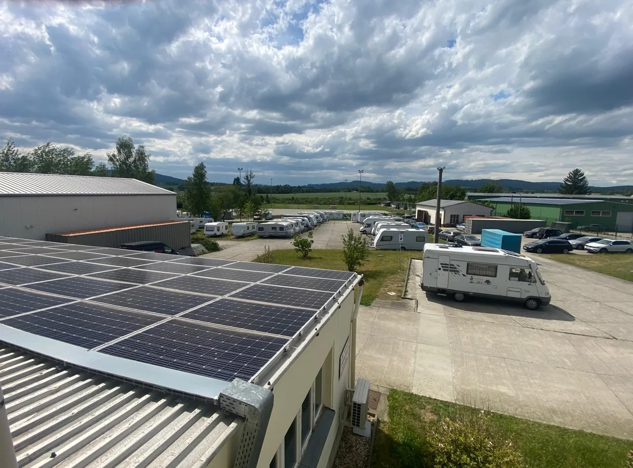 Betriebsgelände mit Wohnmobilen, Wohnwagen, Gebäuden und Solarmodulen im Vordergrund.